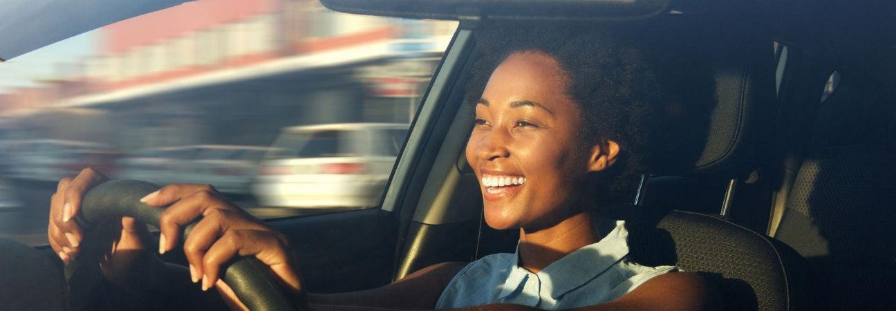 A smiling woman driving through city traffic.